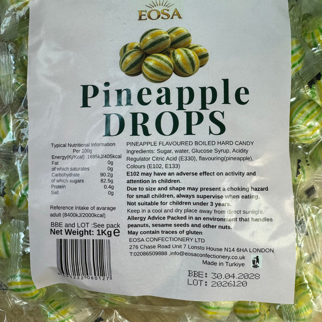A 1kg bag of Eosa Pineapple Drops hard candy in a white bag with green text and a pineapple graphic, photographed against a background of green wrapped candy bags.