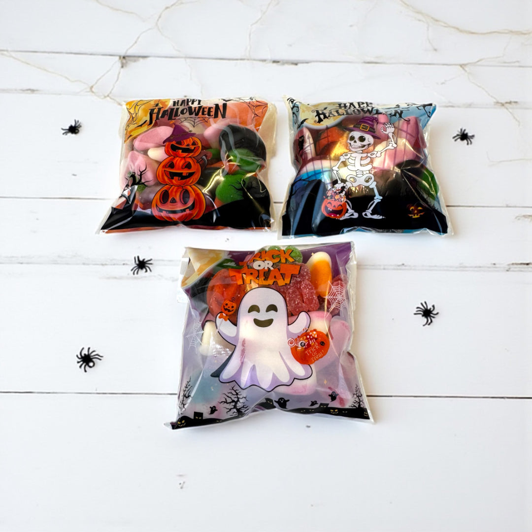 Three Halloween-themed candy bags on a white wooden surface with spider decorations.