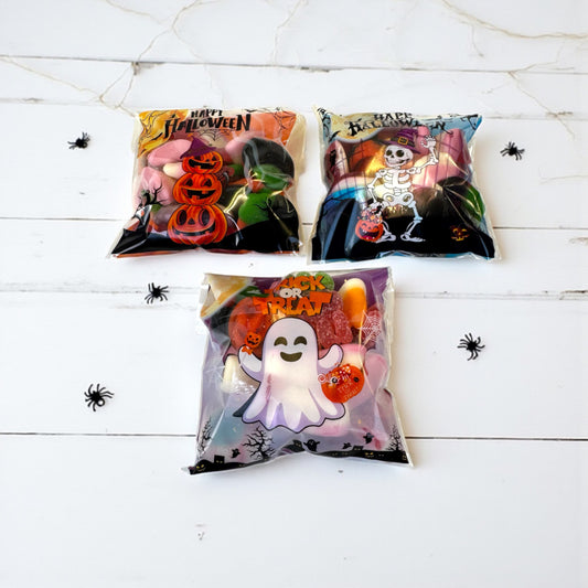Three Halloween-themed candy bags on a white wooden surface with spider decorations.