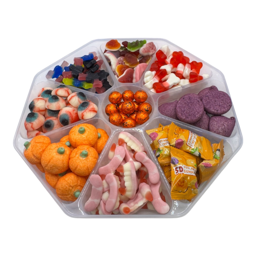 A clear plastic hexagonal candy tray filled with assorted Halloween-themed gummy candies, including orange pumpkin-shaped gummies, pink and white gummy worms, purple gummy bears, orange wrapped candies, and other colorful gummies, on a white background.