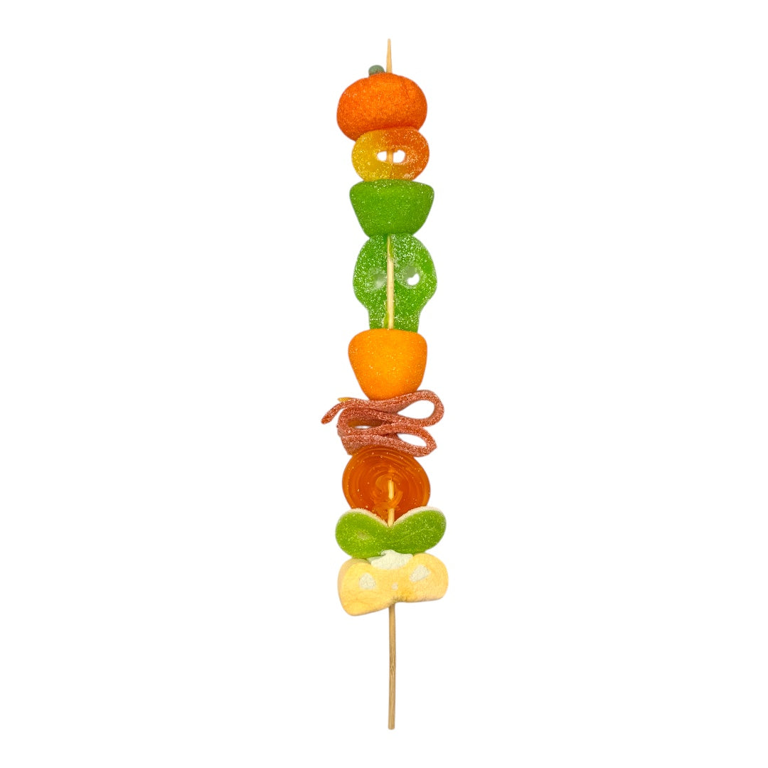 A single skewer of coloruful fruit and candy pieces on a plain white background. Halloween Pumpkin Candy Kebab
