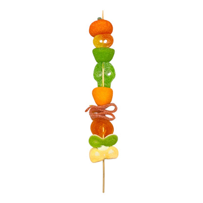 A single skewer of coloruful fruit and candy pieces on a plain white background. Halloween Pumpkin Candy Kebab