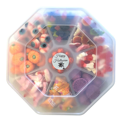 An octagonal clear plastic container filled with assorted Halloween-themed candies and gummy sweets, including orange pumpkins, purple candies, pink gummy worms, and a central round sticker that reads 'Happy Halloween'.