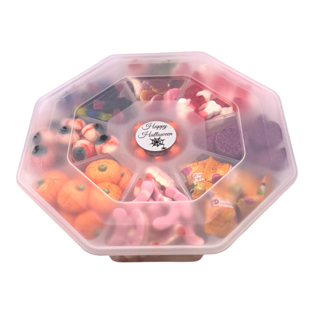 A clear octagonal plastic container filled with assorted Halloween-themed candies and gummy sweets, including orange pumpkins, pink bats, candy corn, and a central sticker that reads 'Happy Halloween'.