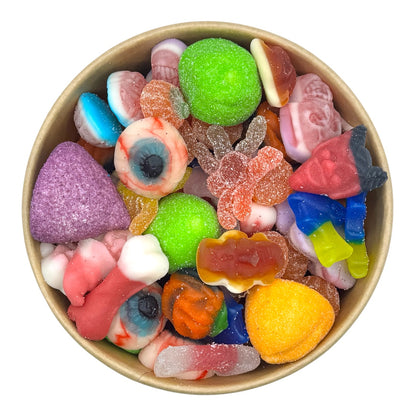 A top-down view of a colorful assortment of gummy and hard candies arranged inside a round kraft paper bowl on a plain white background.