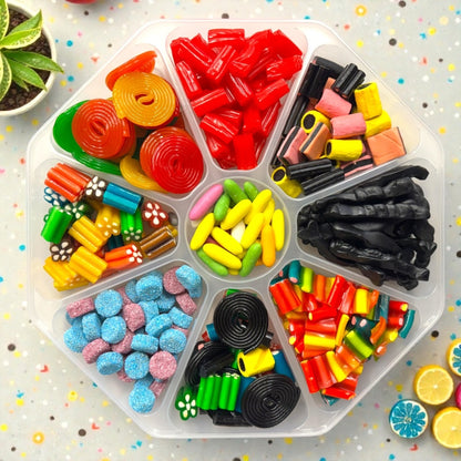 Lollypop Lane sweet platter (with the lid on) filled with an assortment of liquorice sweets on a white table surrounded by succulents.