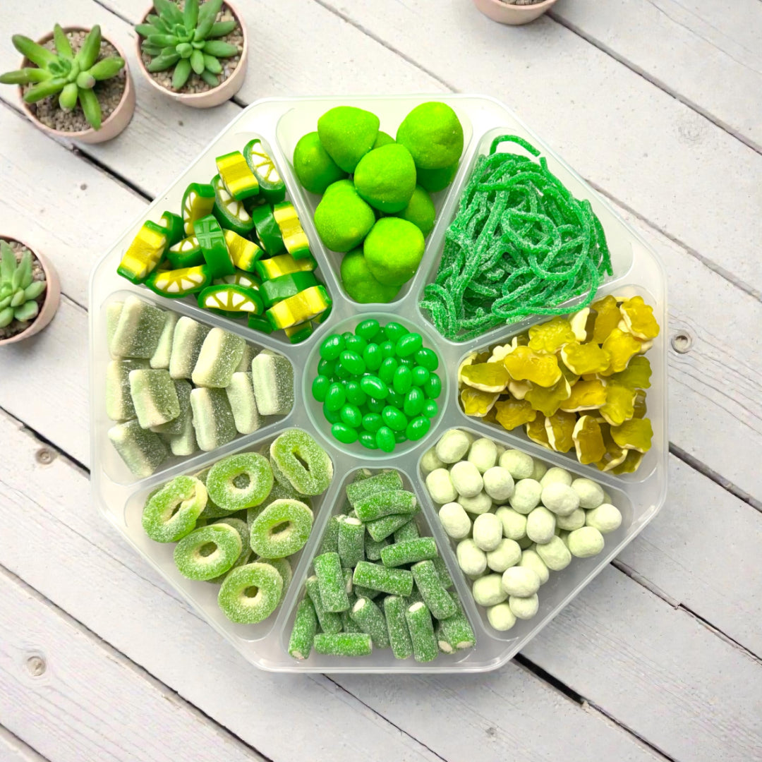 Lollypop Lane sweet platter filled with a selection of green sweets. The platter is on a rustic wooden table surrounded by succulents.