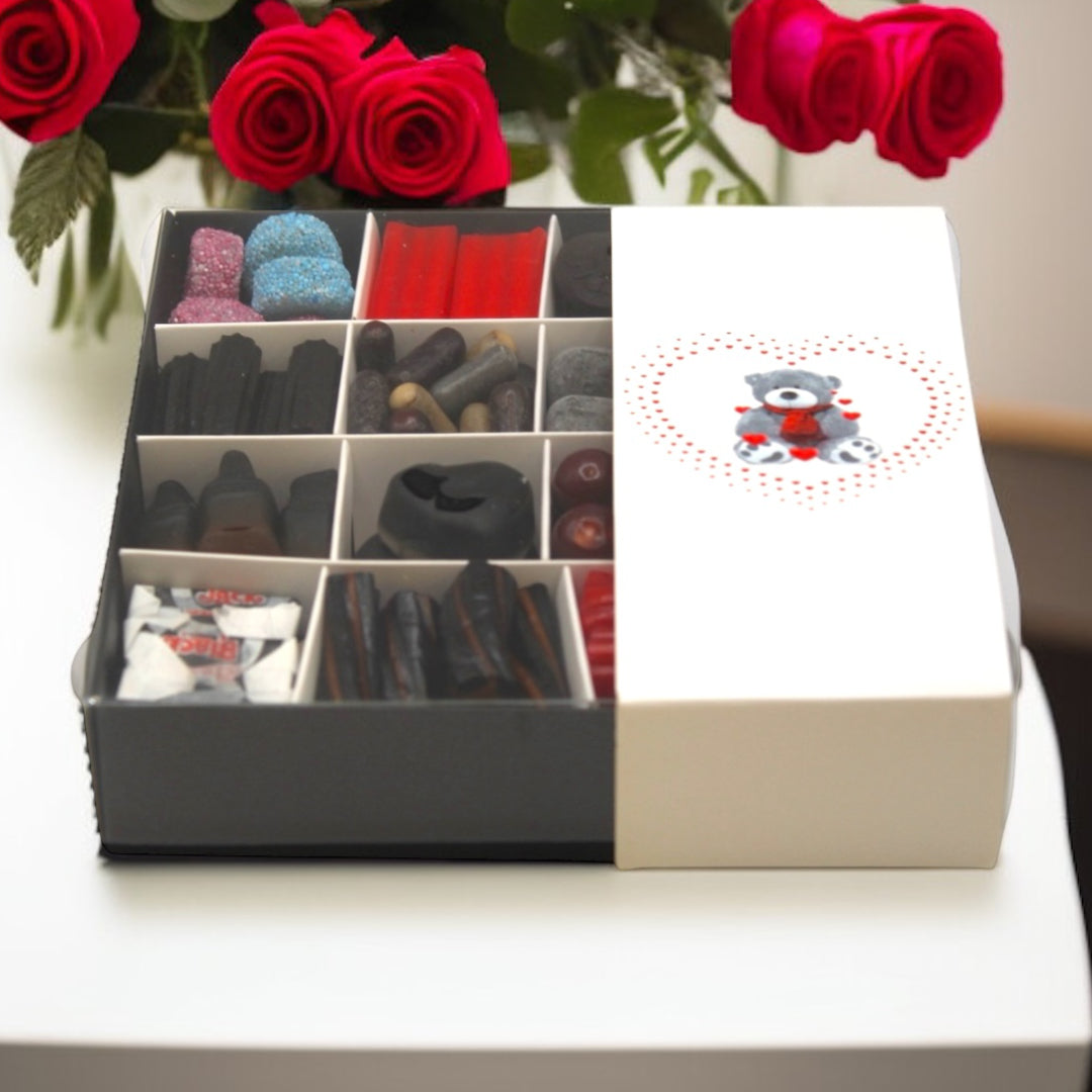 Valentine Liquorice Sweet Gift Box (16 Sweets) on a white table surrounded by roses.