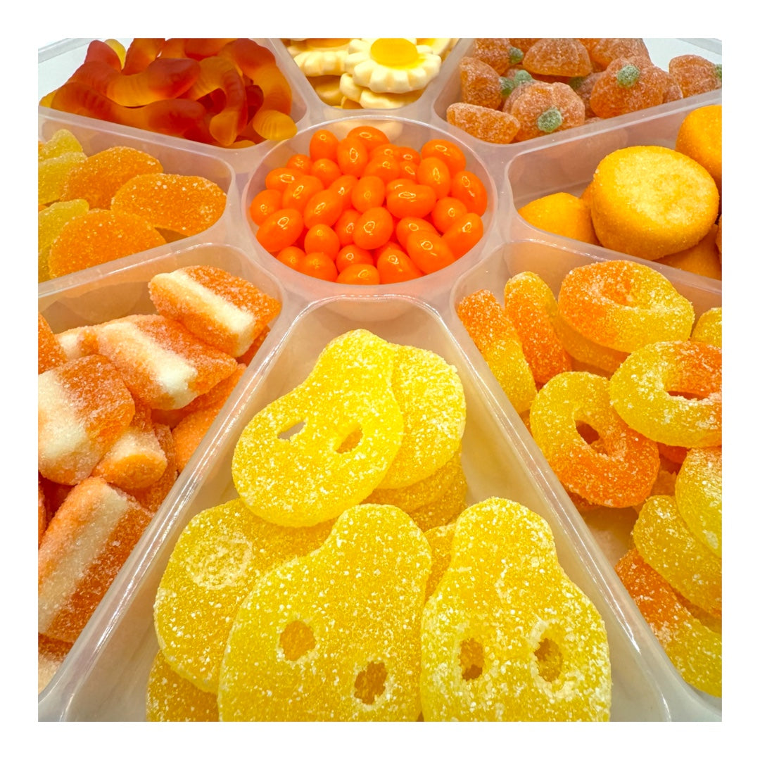 A clear plastic divided candy tray filled with assorted gummy candies in bright colors, including yellow, orange, and white pieces.