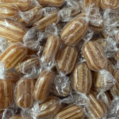 A close-up pile of individually wrapped mint humbugs with a striped pattern of light and dark brown sugar.