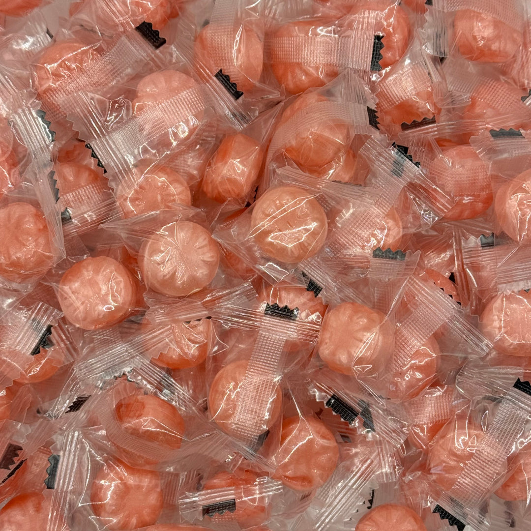 A close-up pile of individually wrapped  Rock Candy Rose EOSA Drops or hard candies in clear plastic packaging with small black printed labels.