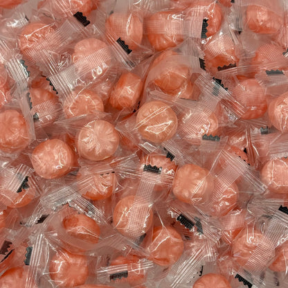 A close-up pile of individually wrapped  Rock Candy Rose EOSA Drops or hard candies in clear plastic packaging with small black printed labels.