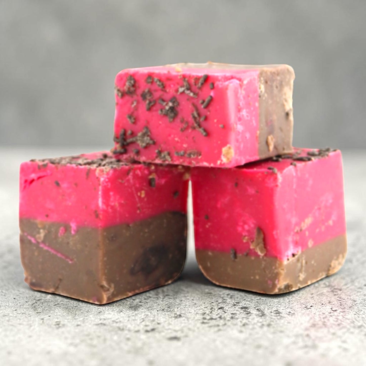 Three square Fudge Factory Black Forest Gateau Fudge stacked together on a gray textured surface.