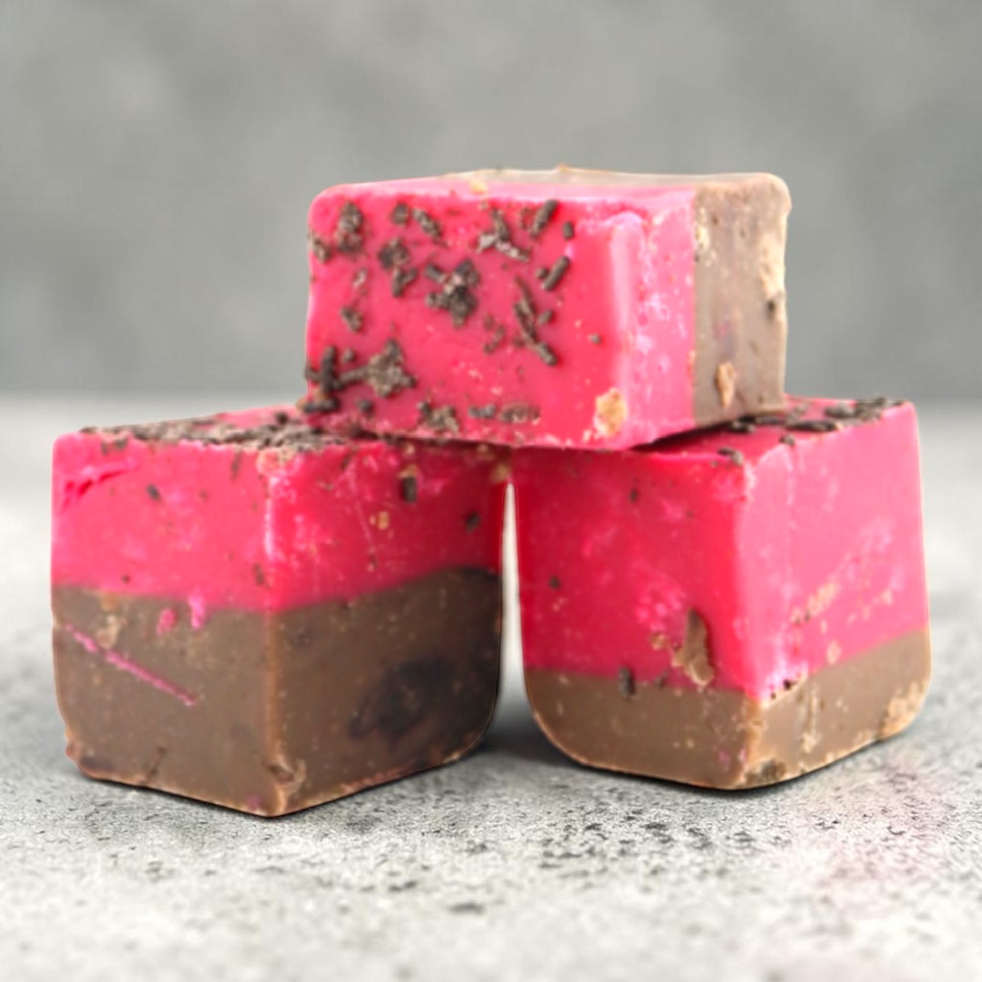 Three square Fudge Factory Black Forest Gateau Fudge stacked together on a gray textured surface.