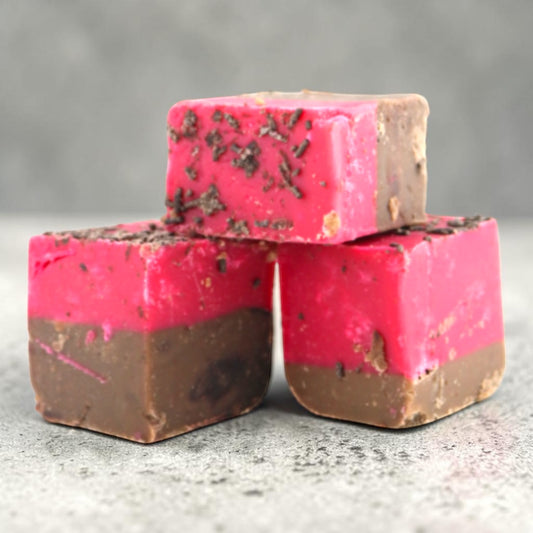 Three square Fudge Factory Black Forest Gateau Fudge stacked together on a gray textured surface.