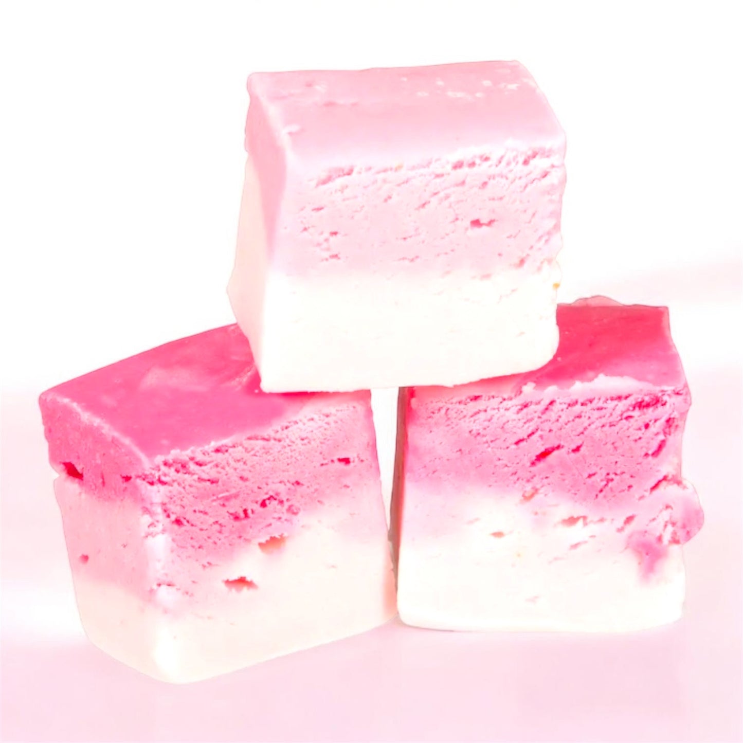 Three chunks of The Fudge Factory Candyfloss Flavoured Nougat on a white and pink background.