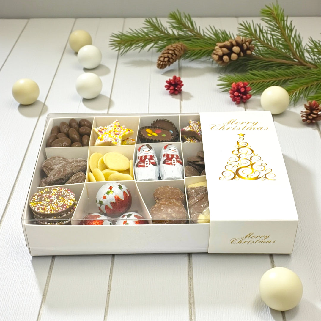 Christmas Gift Box Filled With Chocolate, Gold Tree Logo on a rustic wooden table surrounded by Christmas decor.