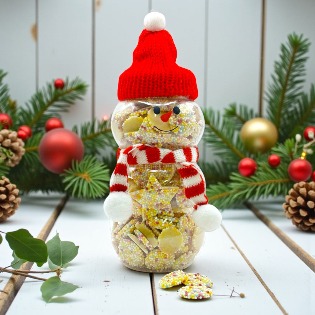 Lollypop Lane Christmas Snowman Jar filled with White Chocolate Snowies and Stars 300g. The background features a rustic wooden table with Christmas foliage.