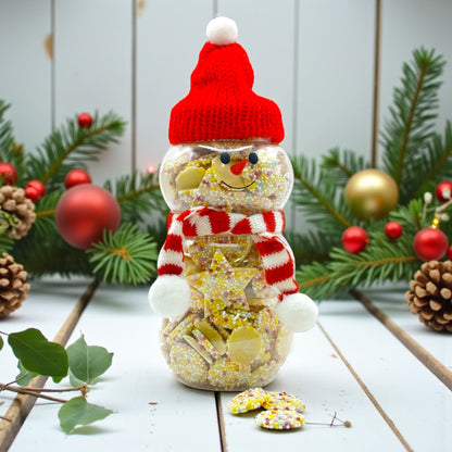 Lollypop Lane Christmas Snowman Jar filled with White Chocolate Snowies and Stars 300g. The background features a rustic wooden table with Christmas foliage.