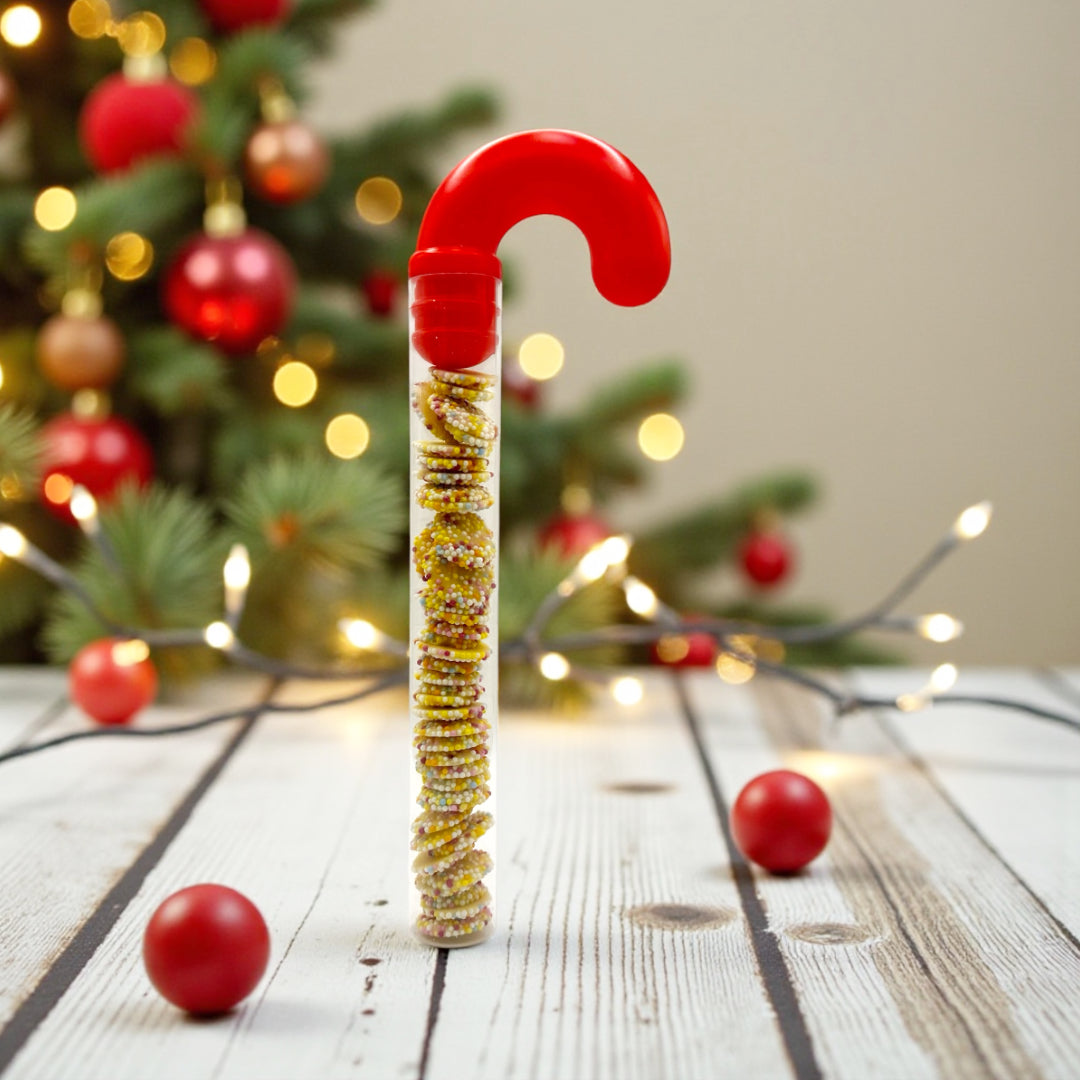 Lollypop Lane Candy Cane filled with White Chocolate Snowies. The background features a wooden table with Christmas decor.